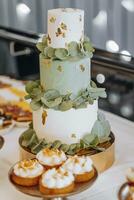 un tres niveles color menta Boda pastel decorado con verde hojas y despojos mortales soportes en un mesa en un restaurante foto