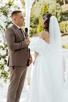 sensible ceremonia de el novia y novio. un contento recién casado Pareja es en pie en contra el antecedentes de un Boda arco, ella dice si a a él. Boda votos el emocional parte de el Boda foto