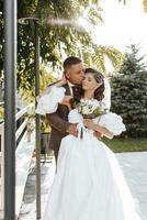 adulto novio en marrón traje abrazando novia en elegante vestir y besos al aire libre en puesta de sol luz, boda, casamiento, relación, estilo de vida foto