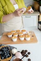 cropped shot of woman pouring milk into cupcakes with blueberries photo