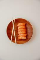 Sushi en un de madera plato con palillos en un blanco antecedentes foto