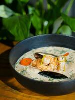 Creamy soup with shrimps and mussels in a black bowl photo