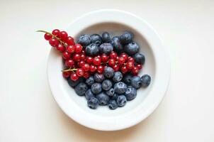 Blueberries and red currants in a bowl on a white background photo