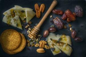 Cheese platter with nuts, raisins and honey on black background photo