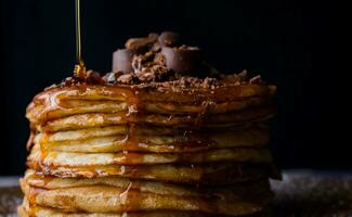 Stack of pancakes with chocolate and caramel on black background, closeup photo