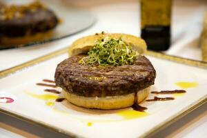 Beef burger on a plate with sauce and sprouts in the background photo
