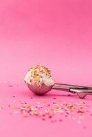 Vanilla ice cream scoop with colorful sprinkles on pink background. photo