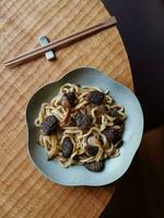 Udon noodles with mushrooms in a plate on a wooden table. photo
