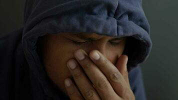 sad man in hood cover face with hands isolated in black. video