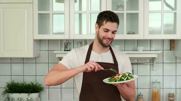 veganistisch Koken, mannetje chef, gezond aan het eten, voedsel levering. een aantrekkelijk Mens in een schort smaakt een gekookt veganistisch salade en geniet het. video
