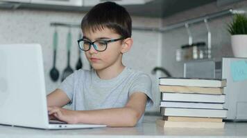 retrato. el niño en lentes lo hace deberes utilizando un ordenador portátil mientras sentado a hogar en el cocina a el mesa. en línea tecnología video