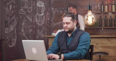 Man with long hair and beard works remotely and is getting a fresh coffee. Waiter bringing a coffee to a freelancer customer. Smiling and enjoying his work. video