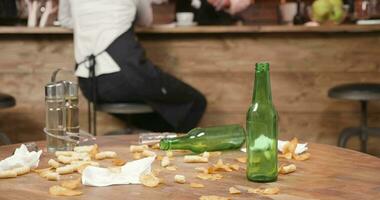 patata papas fritas, servilletas y maíz queso bocanadas en un de madera mesa. vacío botellas izquierda en un sucio mesa en un cerrado restaurante. video