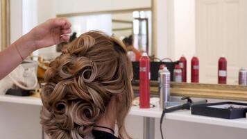 Back view of hairstyling process in a modern saloon next to a mirror video