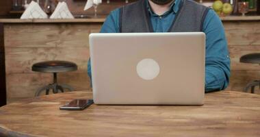 Waiter of a coffee shop brings a cup of coffee and puts it on the table. Customer working on his laptop ordered a cup of fresh espresso. video