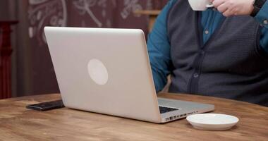 man drycker en bit av espresso medan arbetssätt på hans bärbar dator. avlägsen arbete på en bärbar dator på en trä- tabell och njuter kaffe. video