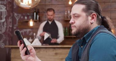 hombre mirando a su teléfono pantalla un poco preocupado. largo peludo hombre enfocado en su teléfono inteligente pantalla. video