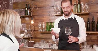 Beau Jeune barbu barman écoute à le serveuse à le bar. nettoyage une verre de du vin et avoir une conversation. video