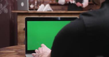 Close up shot Businessman typing fast on a computer with green screen in a vintage pub or restaurant. A bartender sits at the bar counter in the background video