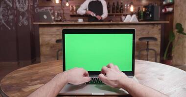 pov Disparo de mecanografía en un ordenador portátil con verde pantalla monitor en un acogedor cafetería, pub o restaurante video