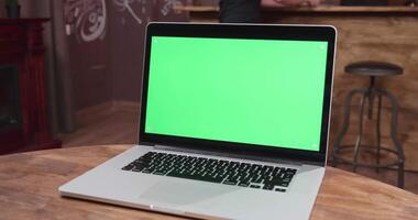 Modern laptop sits on a wooden table in vintage rustic pub. You can replace the green screen with your own site, app or footage video