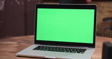 Parallax shot of modern laptop with green screen on the display. A vintage barcounter is in the background video