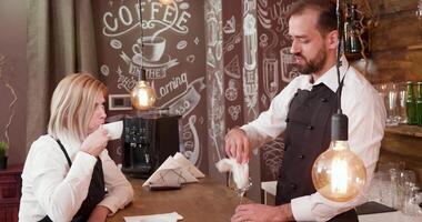 Handsome bartender in black apron talks with the waitress. Coworkers take a break during a busy day at the restaurant. video