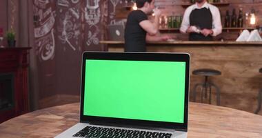 Laptop with green scree on a table in a vintage restaurant. Easy replace the green screen with your graphics, photos, videos or website.