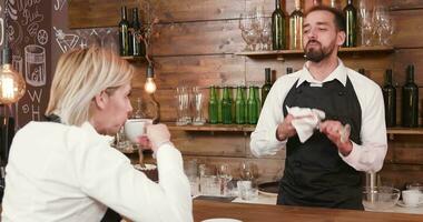 manlig bartender samtal till de servitris medan rengöring en glas. kvinna servitris på de bar disken dricka kaffe. video