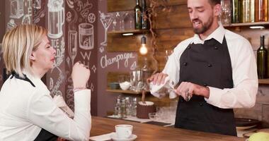 Pretty waitress at the bar counter talks to a handsome bartender. Interior of a small vintage style coffee shop. video