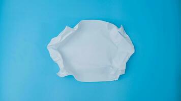 A paper ball is spread out into a blank sheet on blue background. Crumpled blank white paper with copy space for text or advertising space. photo