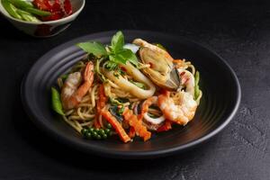 Seafood drunken spaghetti with shrimp squid clams chili, and basil. Thai food. Healthy Asian in a plate on a black background table. Top view. photo