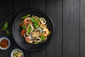 Seafood drunken spaghetti with shrimp squid clams chili, and basil. Thai food. Healthy Asian in a plate on a black background table. Top view. photo