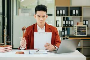 justice and law concept. Asian Male judge in a courtroom the gavel, working with smart phone and laptop and digital tablet computer photo