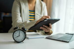 Alarm clock on the desk. Business hand using smartphone, laptop and tablet  working in modern office building photo