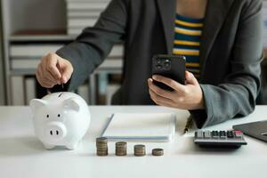 Business woman hand putting money coin into piggy bank with step of growing stack coins for saving money with virtual icon photo