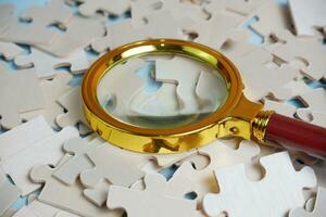 magnifying glass and on the missing puzzle piece. photo illustration concept of searching for and recruiting new employees