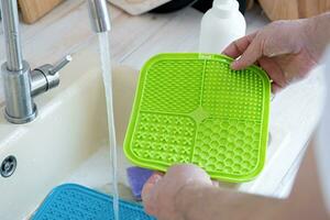 hands washing pet lick mat in kitchen sink photo