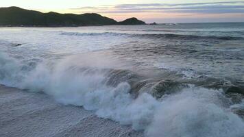 Drohne Aussicht von Sturm Welle abstürzen auf zu sandig Strand und Felsen beim Sonnenaufgang video