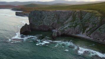 Aerial view of beautiful sea stack and dark cliffs in sunset. Calm seascape video