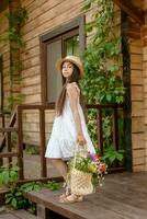 Dark-haired tween girl standing on wooden doorstep with basket of wildflowers photo