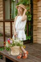 Playful tween girl standing on doorstep of country house with basket of wildflowers photo