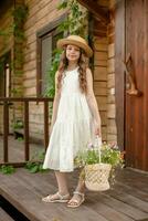 Smiling tween girl standing on doorstep of country cottage with basket of flowers photo