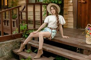 Brown-haired tween girl sitting on wooden doorstep of country house in summer photo