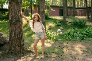 Full-length portrait of tween girl leaning of tree in courtyard of country house in summer photo