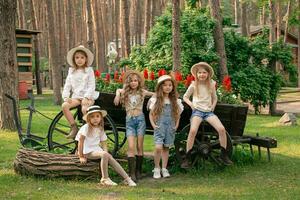 Group of friendly preteen girls posing next to vintage wooden cart designed as flower bed outdoors photo