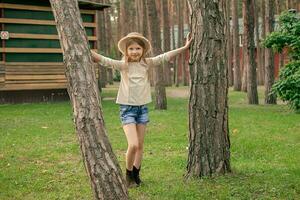 Smiling tween girl standing touching on two trees in green summer courtyard of country house photo