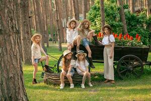 Cheerful preteen girls posing near flower bed in shape of wooden cart in summer park photo