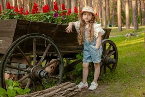 Little girl leaning vintage wooden cart used as flowerbed in summer park photo