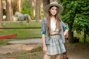 Teenage girl standing near open stable in summer country estate photo